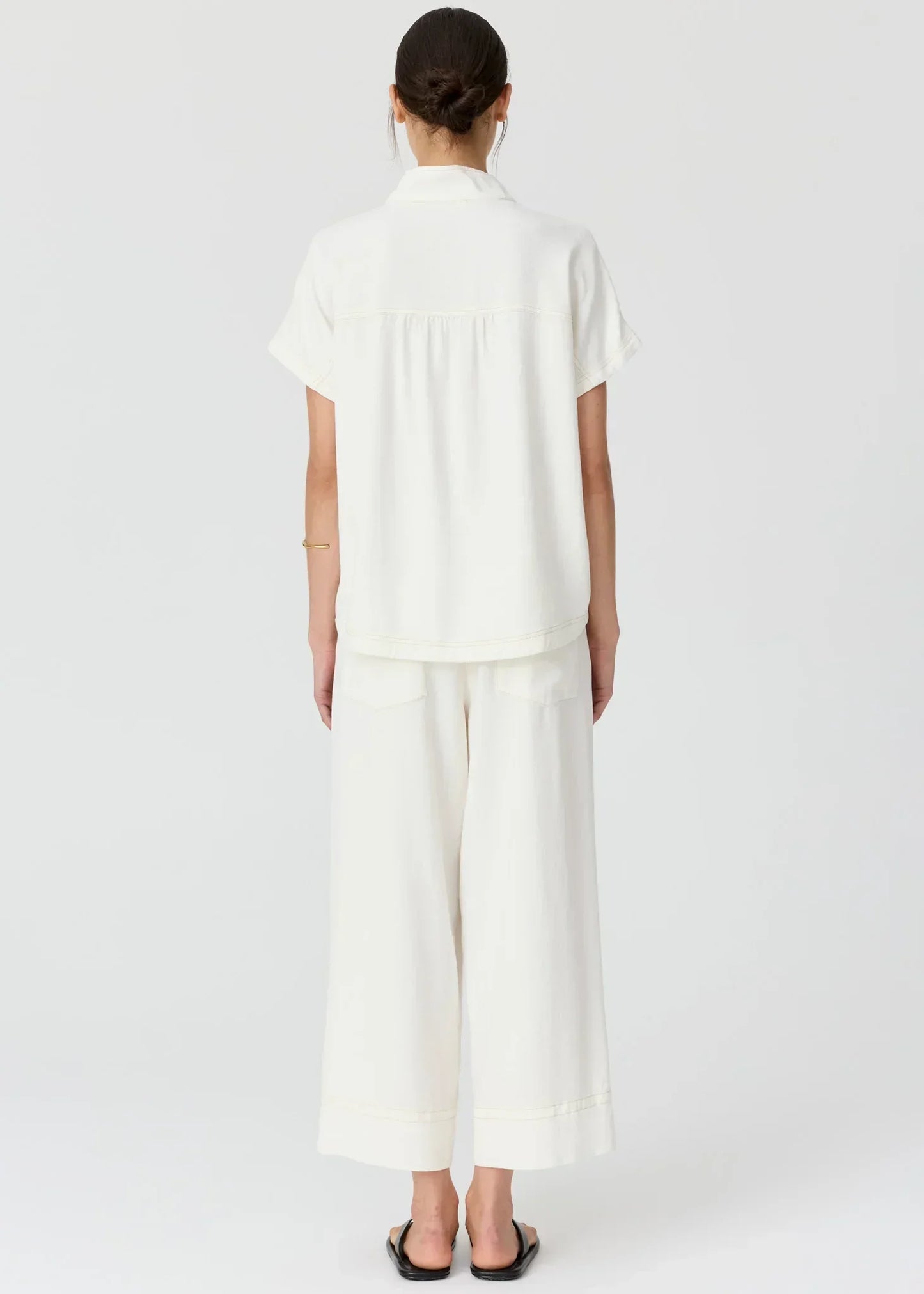 Rear view of a woman wearing a white short-sleeve shirt and matching wide-leg trousers.
