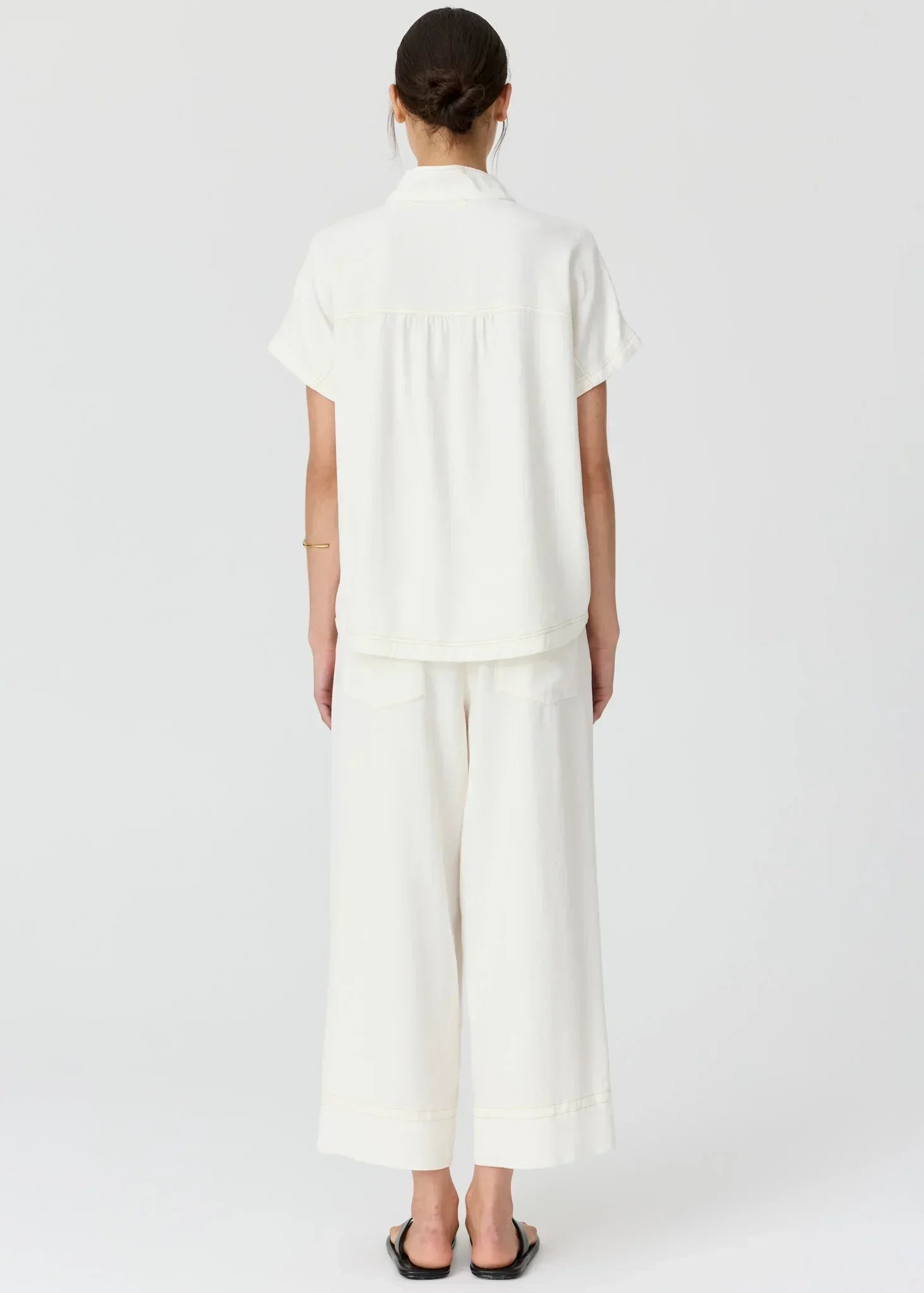 Rear view of a woman wearing a white short-sleeve shirt and matching wide-leg trousers.