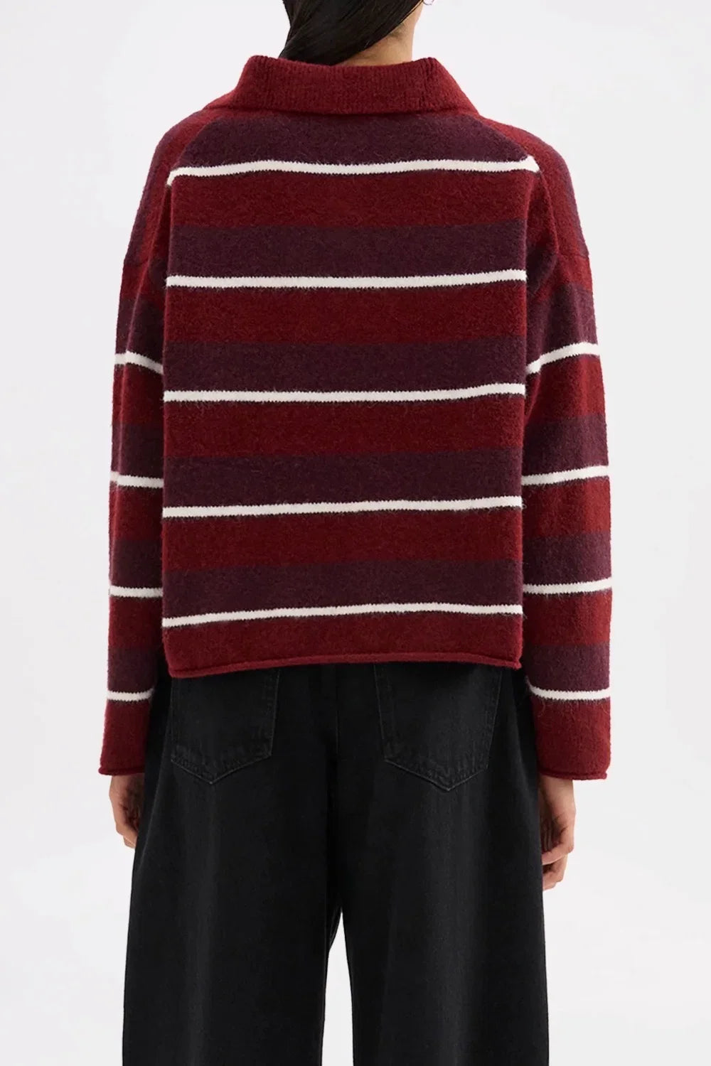 Back view of a woman wearing a burgundy and white striped oversized knit sweater and black pants.