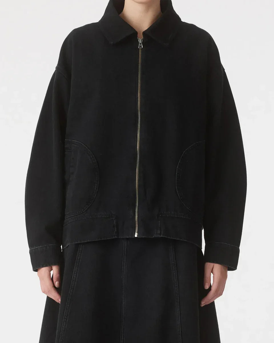 Black oversized denim jacket with front zipper and patch pockets, styled with matching skirt