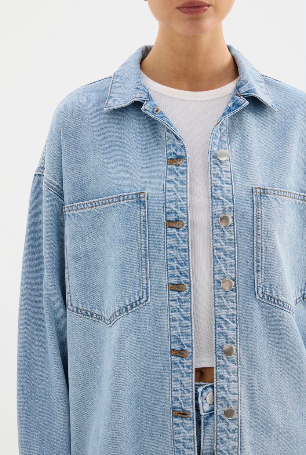 Light blue denim jacket with front pockets and button closure, styled over white ribbed top