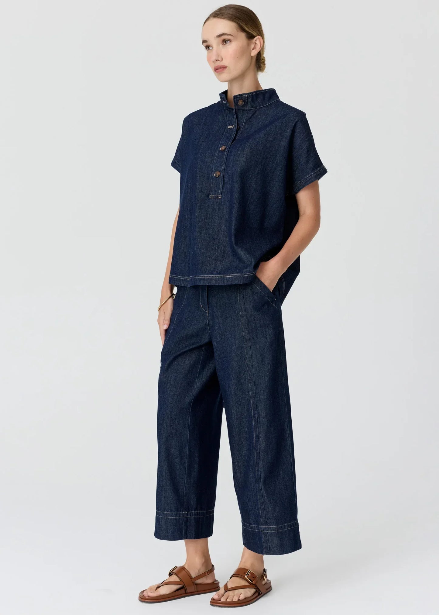 Woman wearing a dark wash denim short-sleeve shirt and matching wide-leg trousers.
