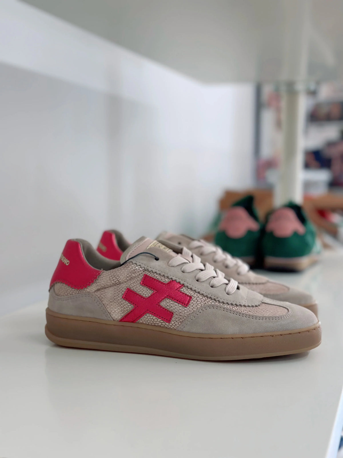 Beige and pink sneakers with a distinct red cross logo on a white shelf.
