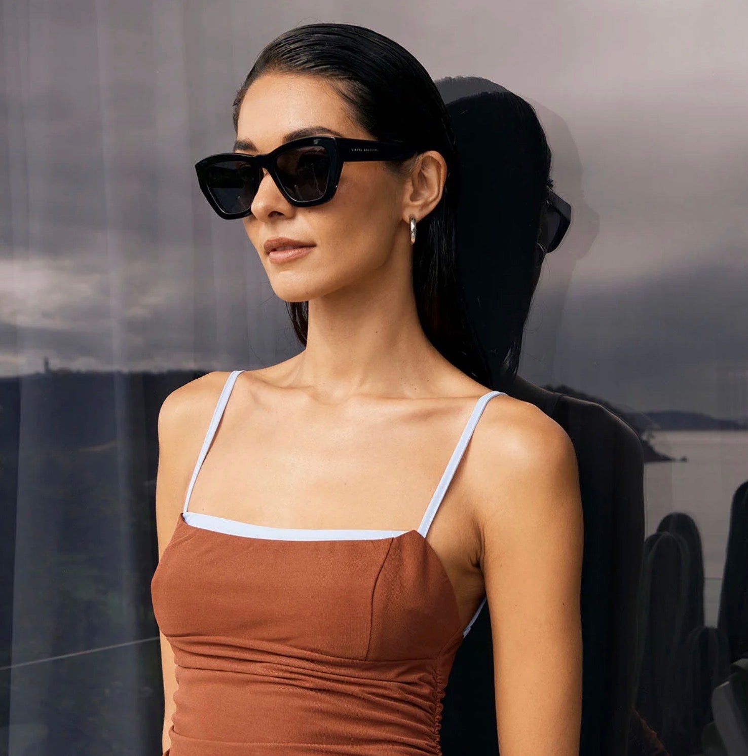 Woman wearing stylish black cat-eye sunglasses and brown ruched top, modern fashion look
