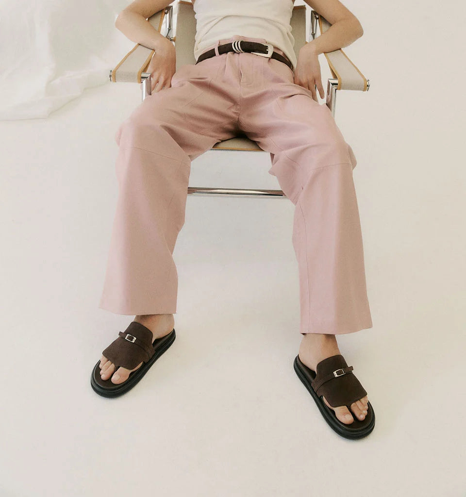 Person wearing pink wide-leg trousers and brown buckle slide sandals sitting in a chair.