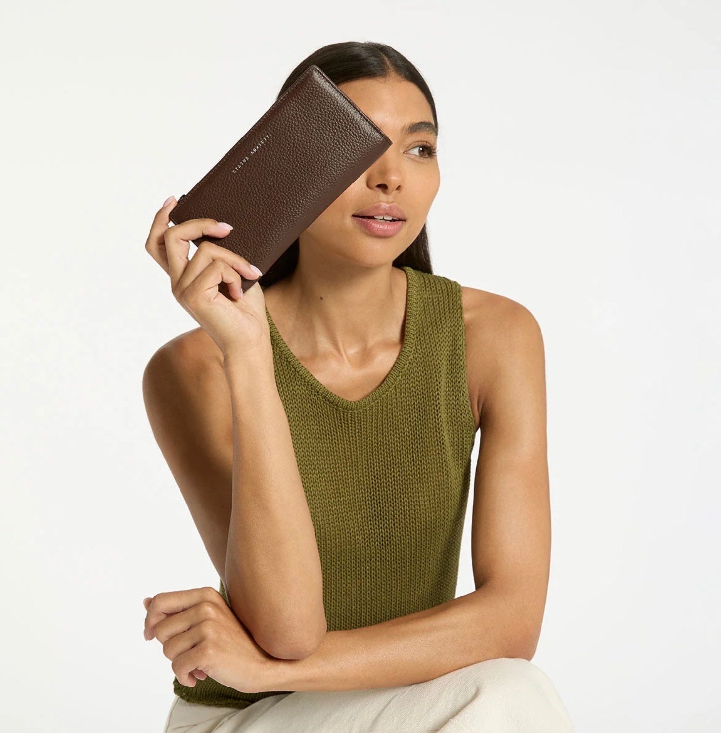 Woman holding brown textured wallet, wearing olive knit top — stylish everyday accessory