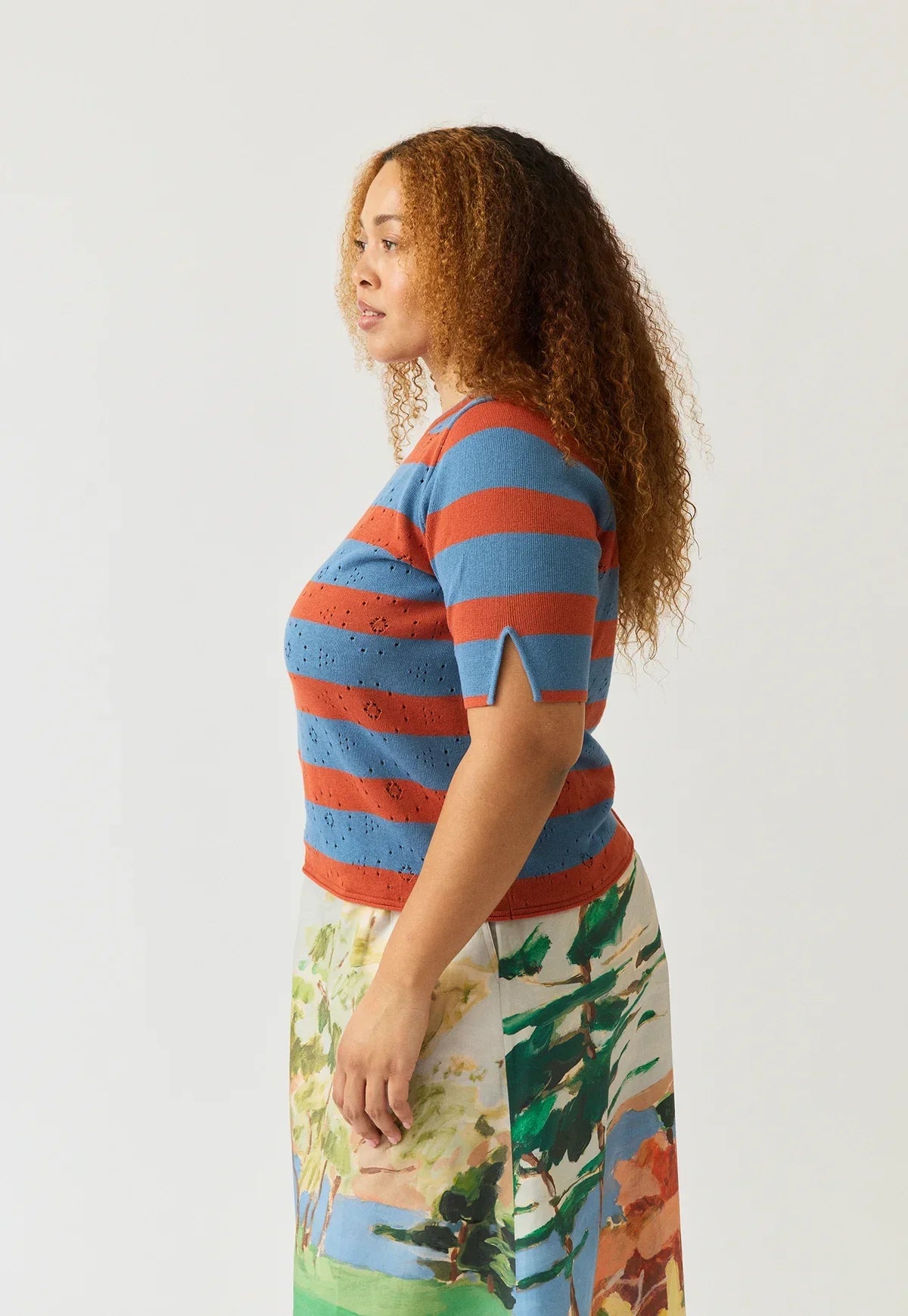 Woman wearing a NANCYBIRD Rana Knit Tee in Terracotta Stripe paired with a patterned skirt.