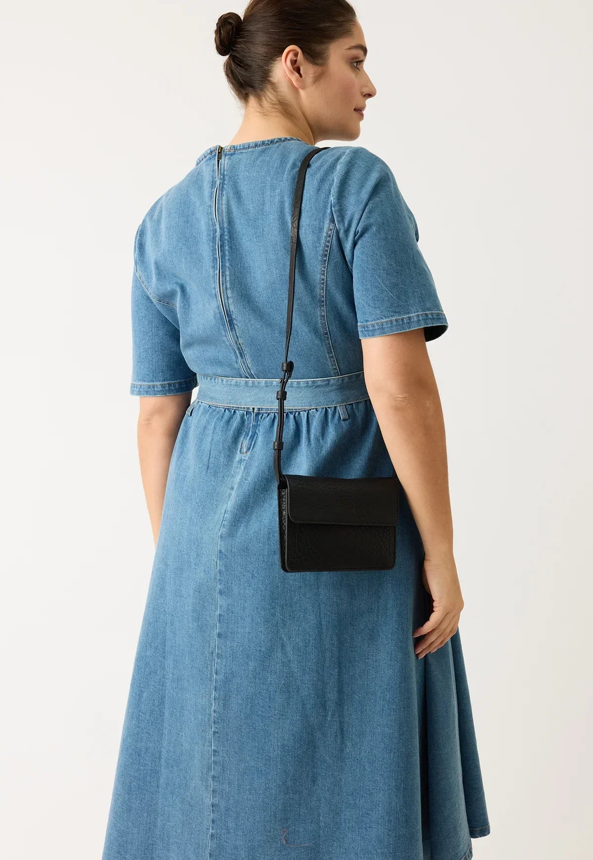 Woman in denim dress with black crossbody bag, fashion accessory on white background
