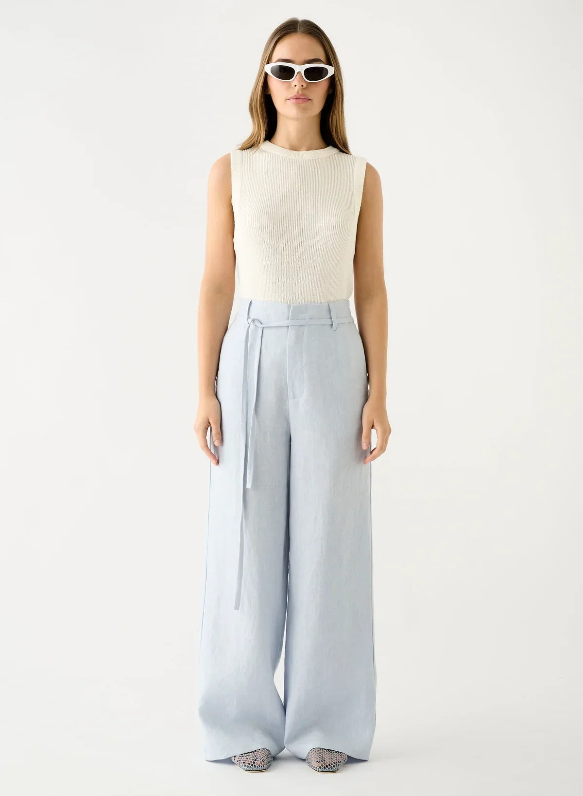 Woman wearing Esmaee Olivia Pant in Ice Blue with a white sleeveless knit top and white sunglasses.
