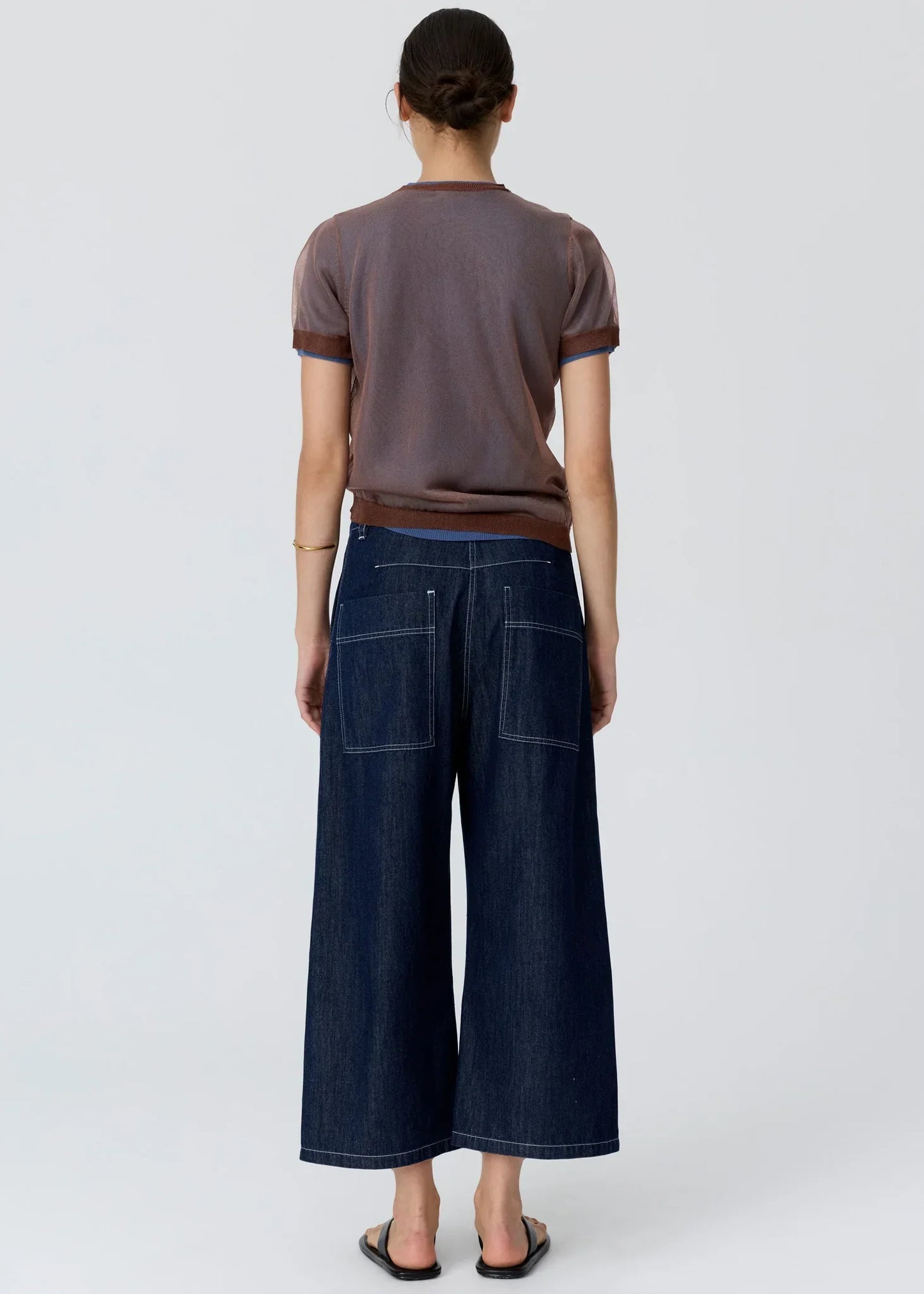 Back view of a woman wearing a brown short-sleeved t-shirt and dark denim wide-leg culottes.