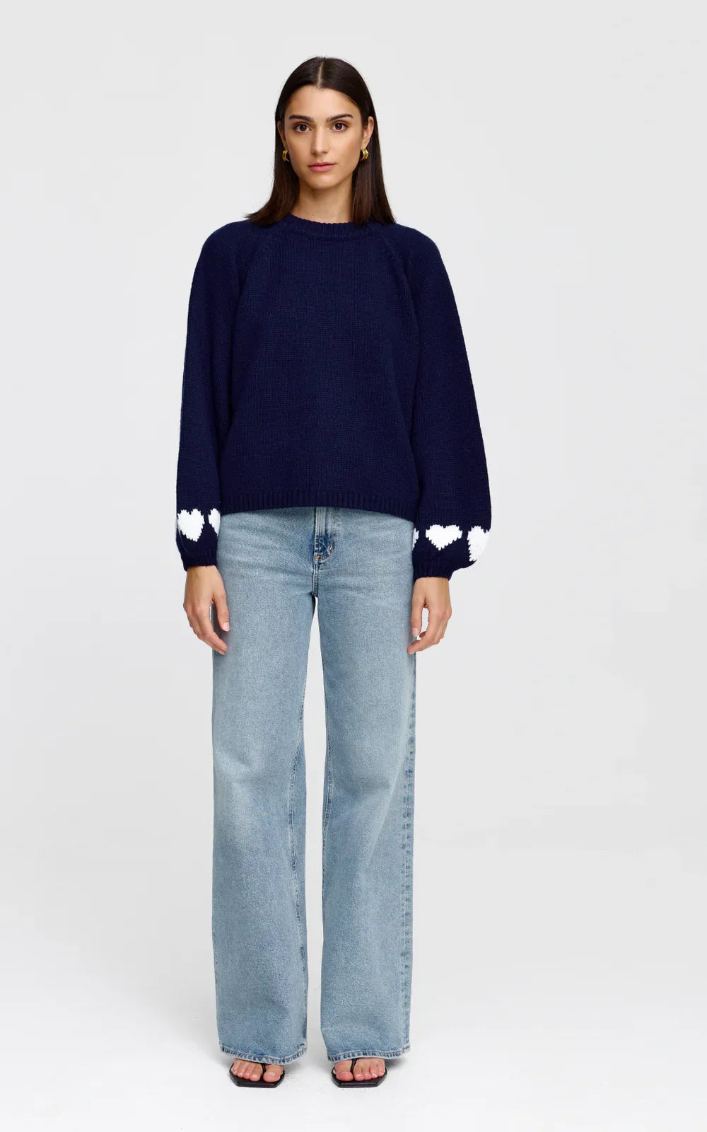 Navy blue knit sweater with white heart details on sleeves, paired with light wash wide-leg jeans