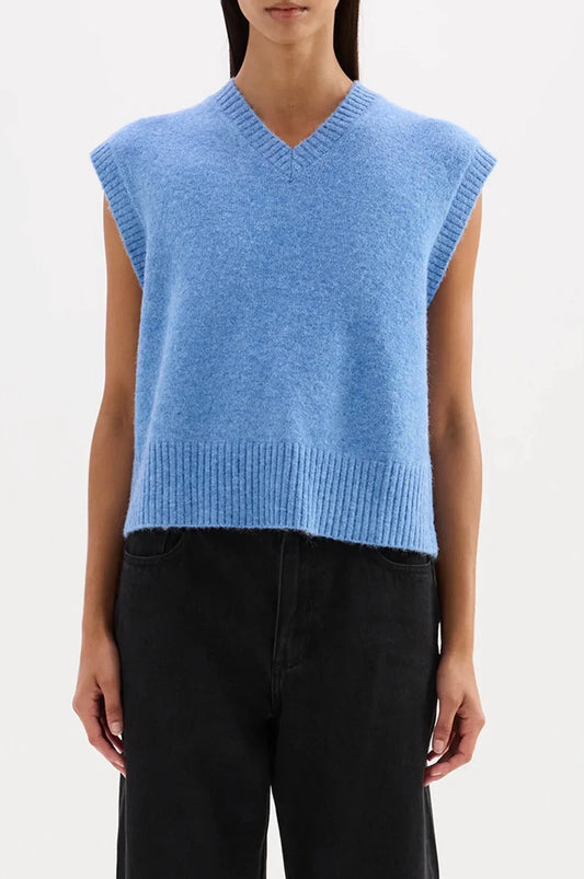 Woman wearing a blue knitted sleeveless V-neck vest with black pants
