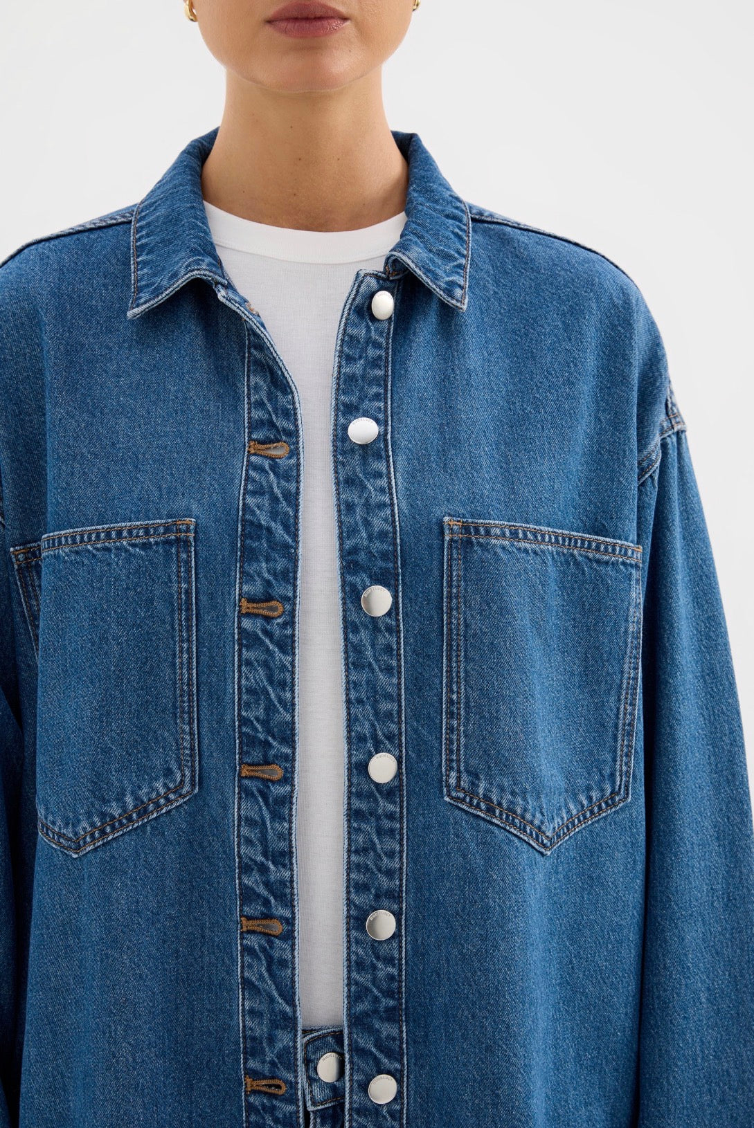 Blue denim shirt with white buttons and front pockets, styled over a white tee
