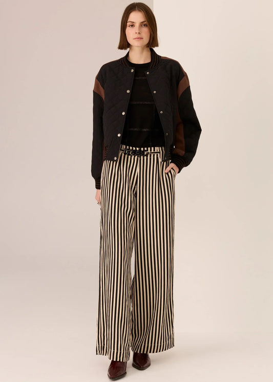 Woman wearing black quilted bomber jacket, striped wide-leg pants, and brown boots