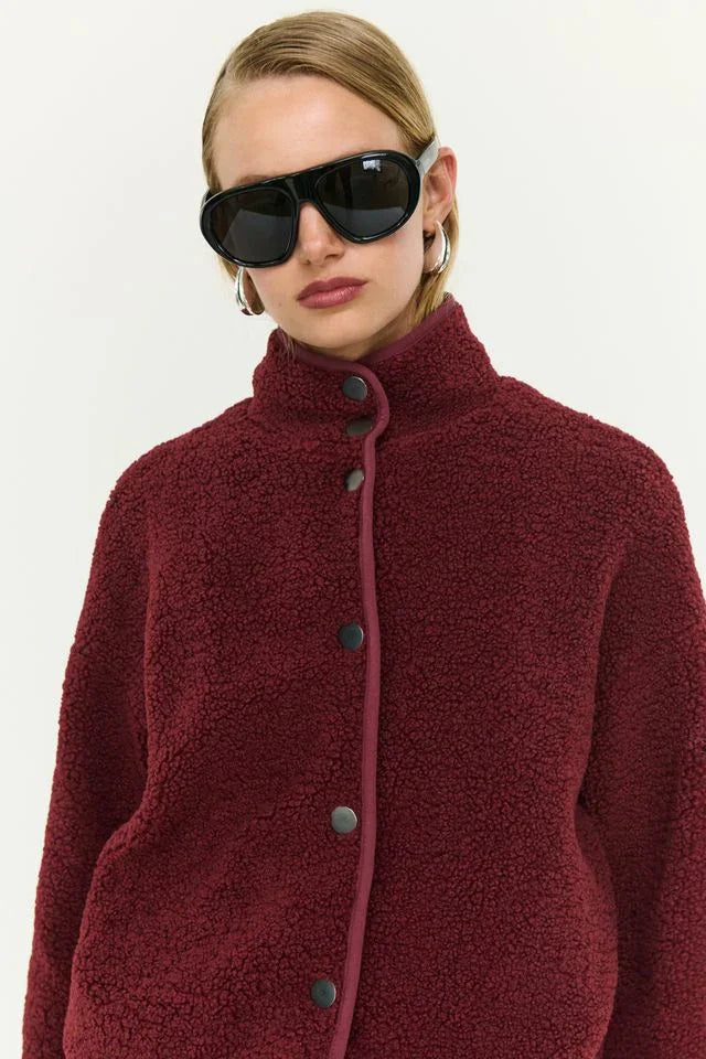 Woman in burgundy teddy coat with high collar and black buttons, styled with oversized sunglasses