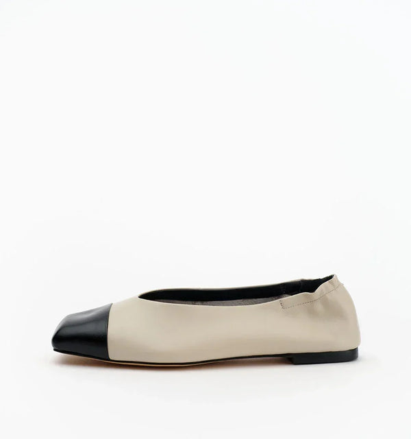 Beige ballet flat with a black cap toe on a white background