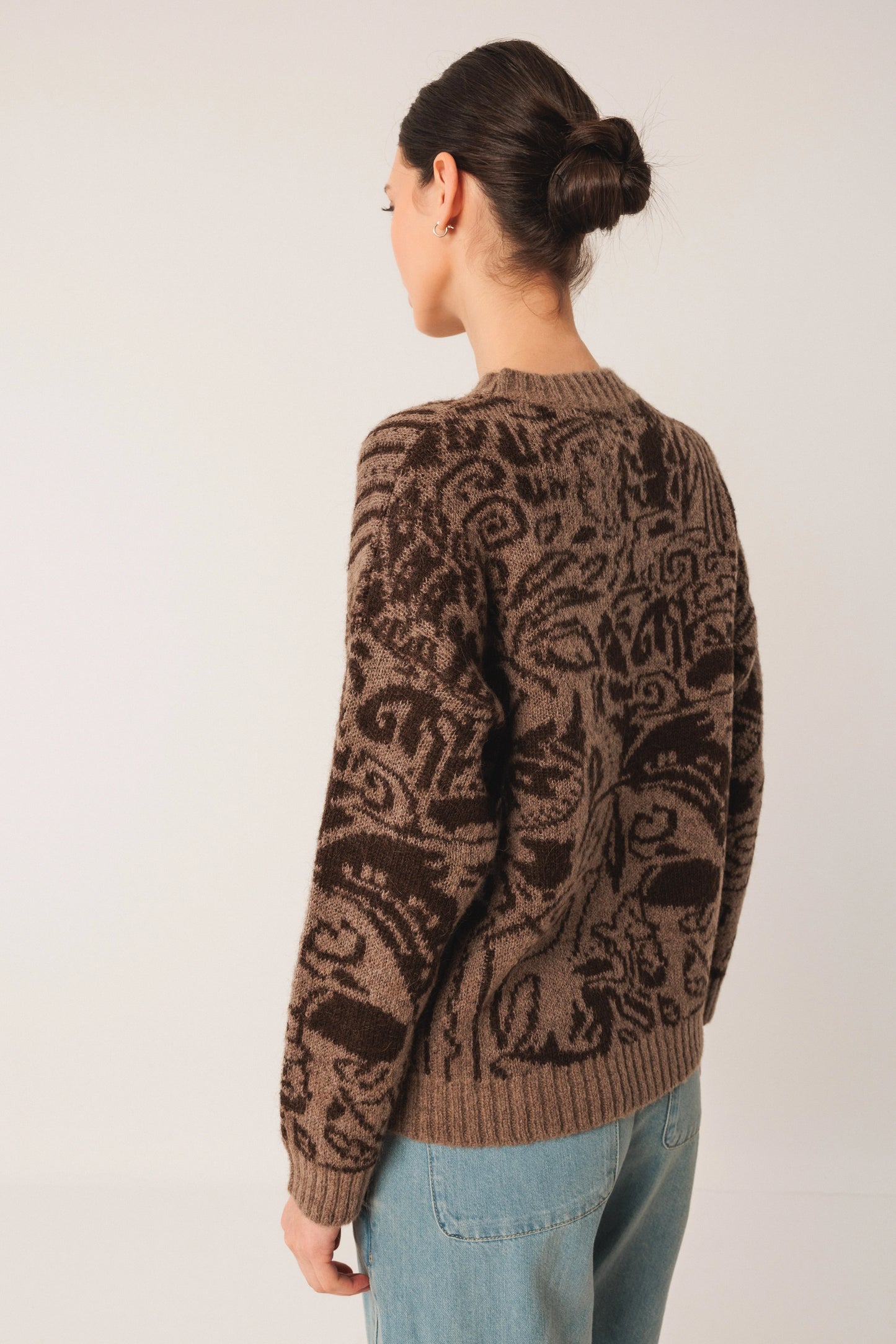 Brown patterned knit sweater with intricate design, worn with blue jeans, back view