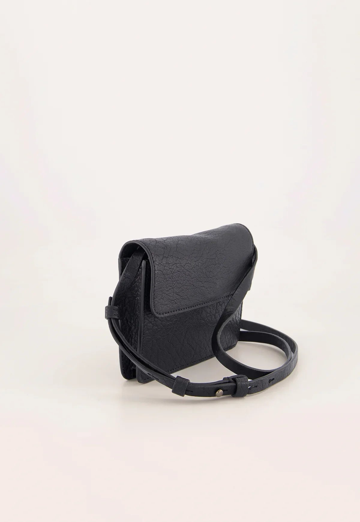 Black textured leather crossbody bag with flap closure and adjustable strap on neutral background