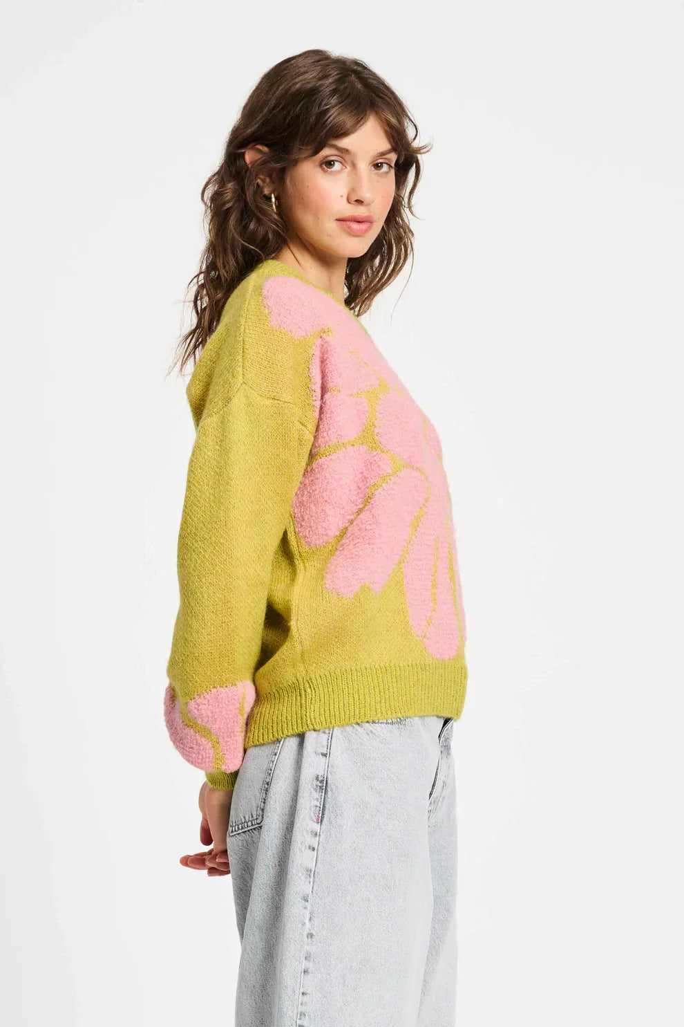 Woman wearing green knit sweater with pink floral pattern and light wash jeans