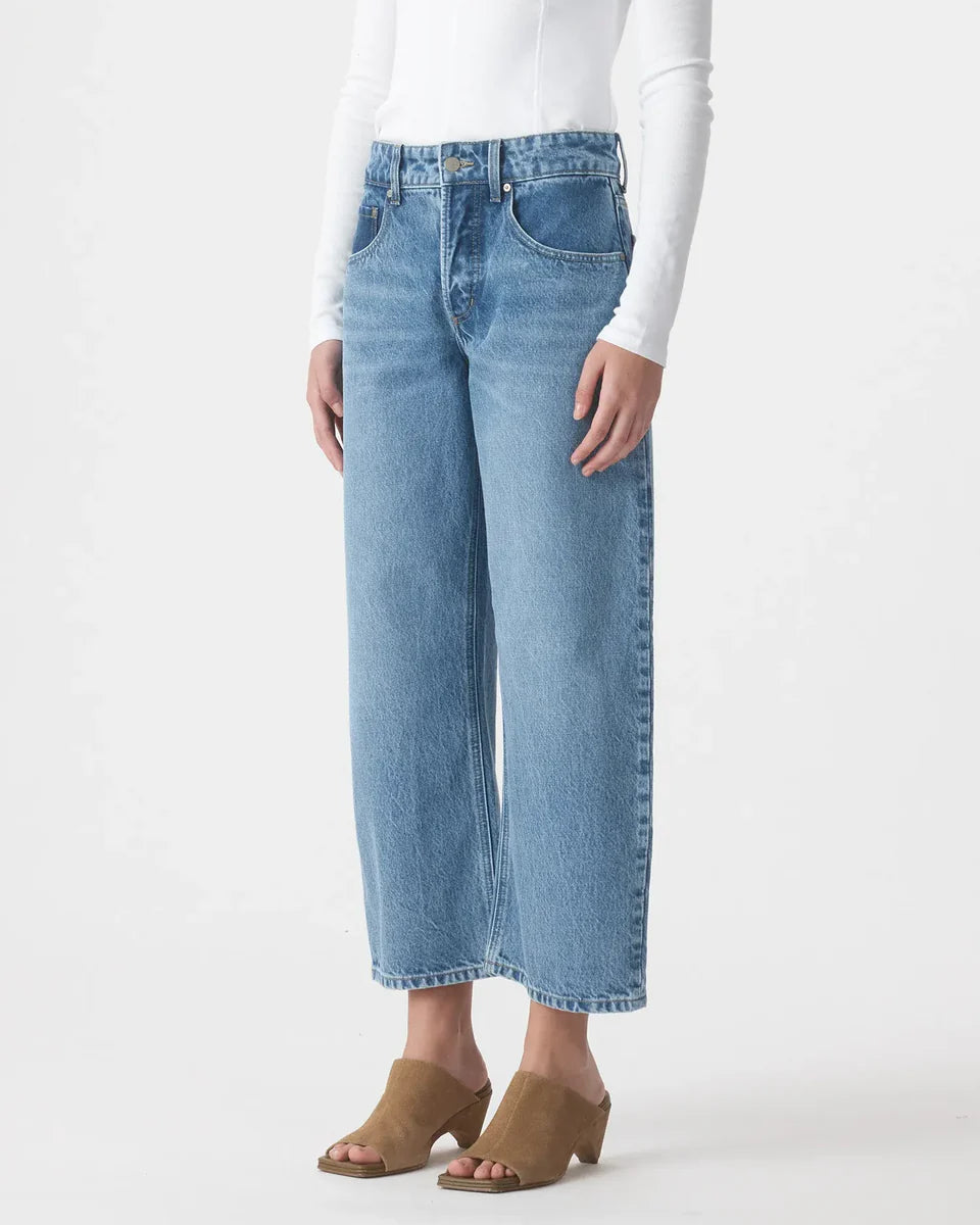 Woman wearing high-waisted wide-leg blue jeans, white top, and tan heeled mules