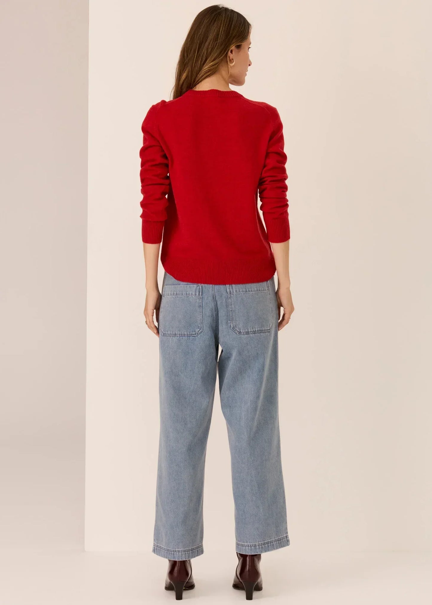 Woman wearing a red knit sweater and wide-leg blue jeans, shown from the back