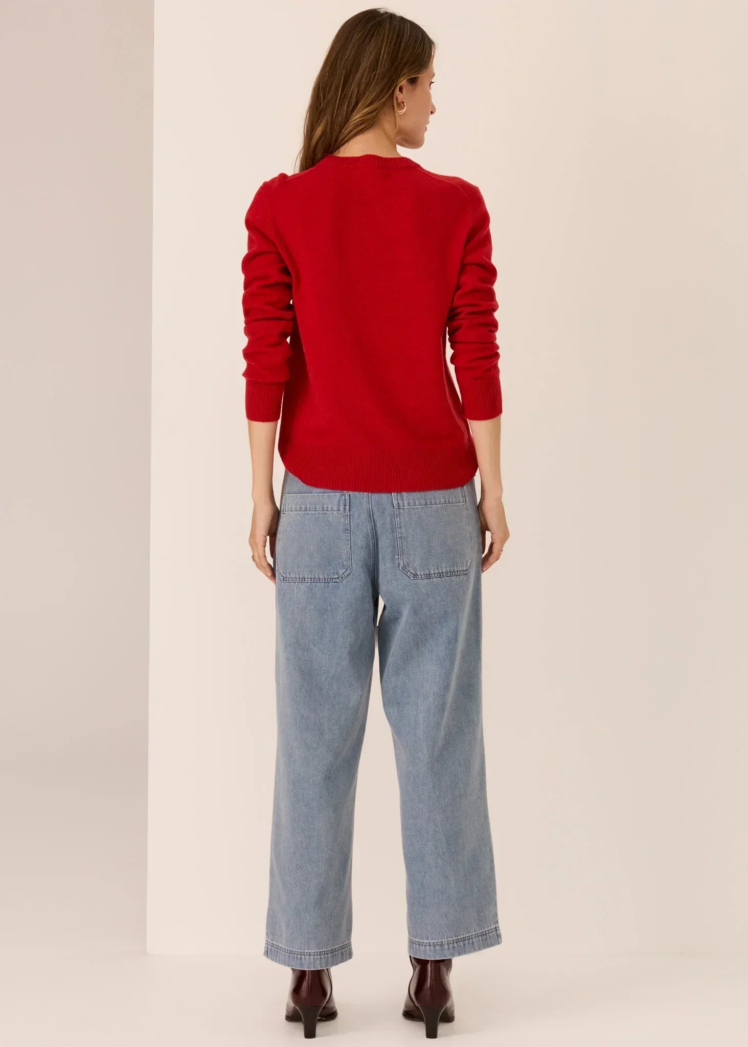 Woman wearing a red knit sweater and wide-leg blue jeans, shown from the back