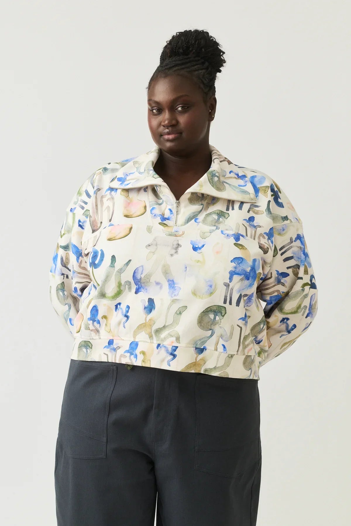 Woman wearing abstract print pullover top with half-zip and dark high-waisted pants