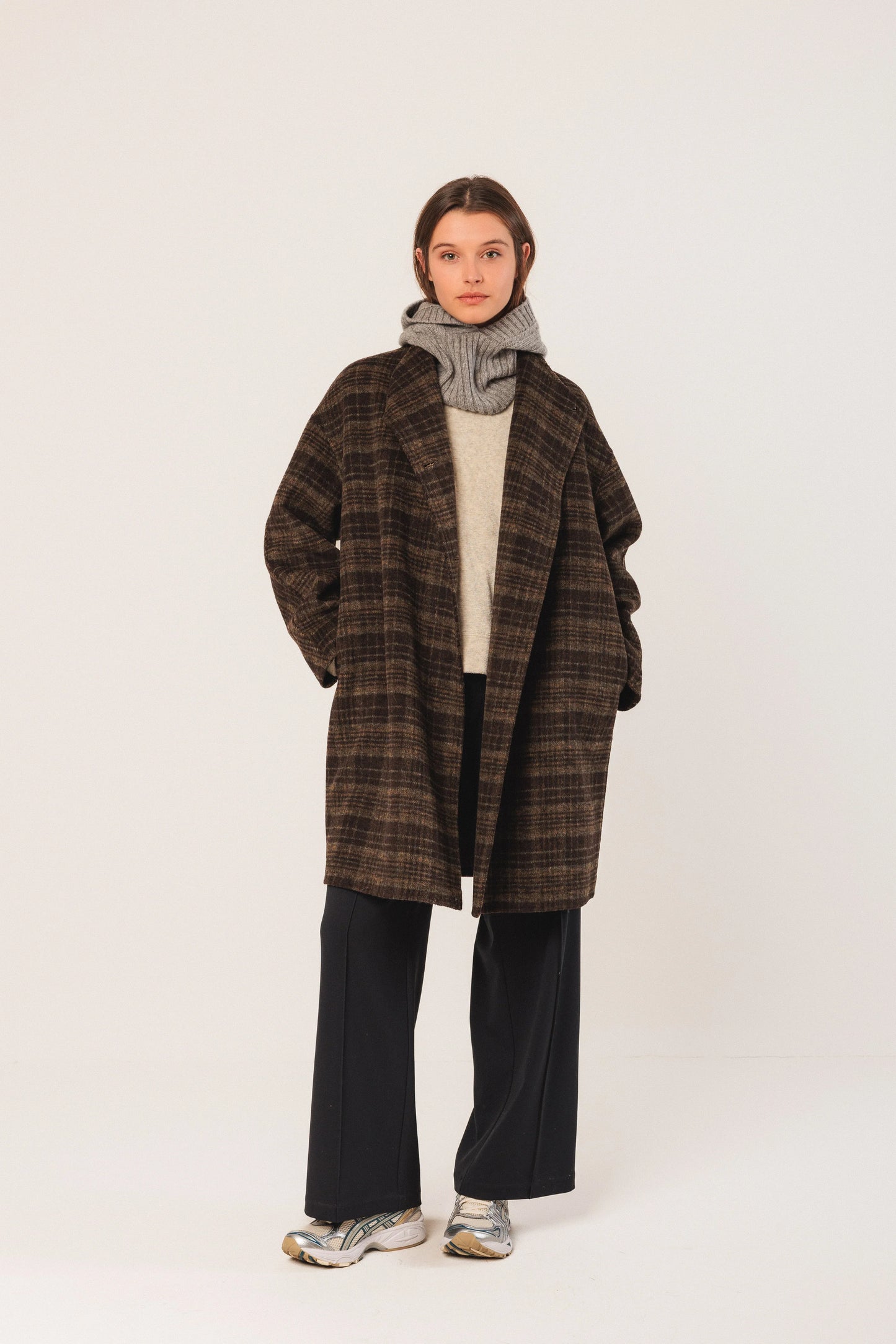 Woman wearing brown plaid coat, gray scarf, and black wide-leg pants with sneakers