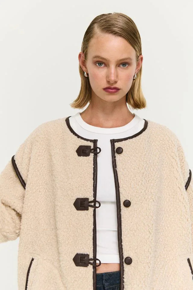 Cream shearling coat with brown trim and toggle buttons, styled with white top and jeans