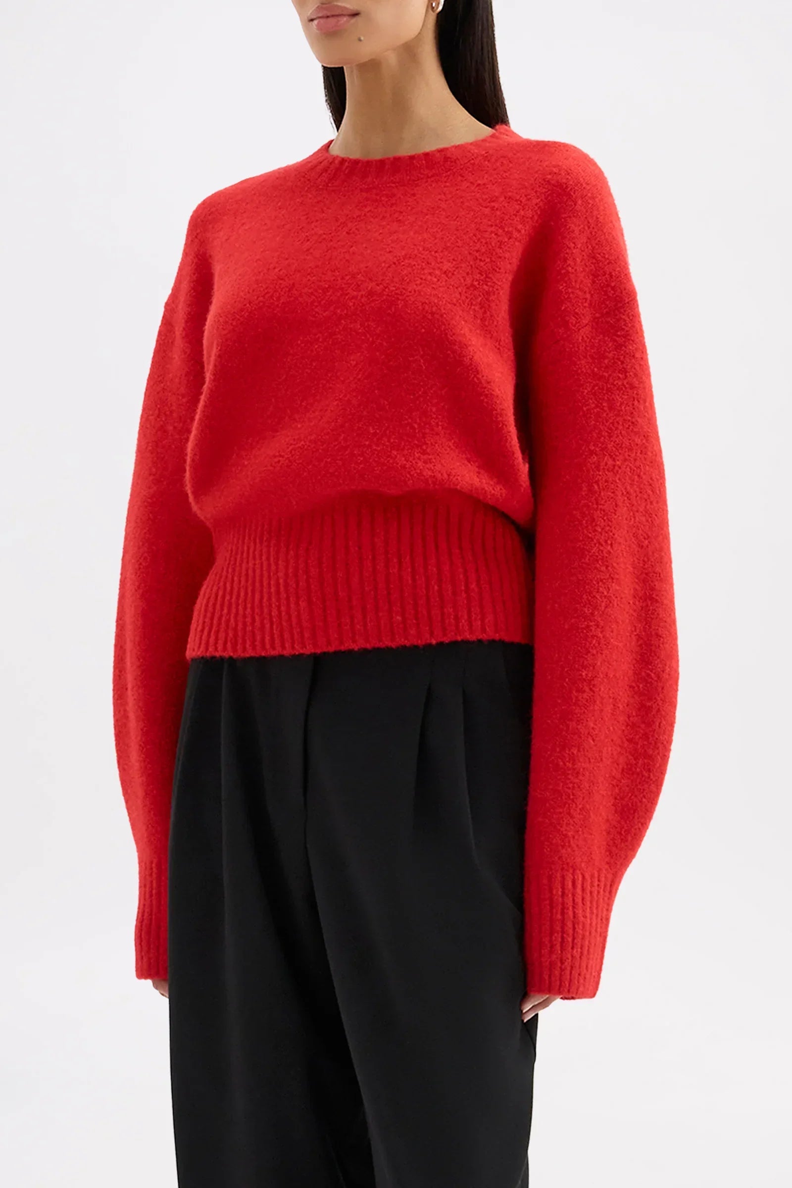 Woman wearing a bright red oversized knit sweater and black trousers.