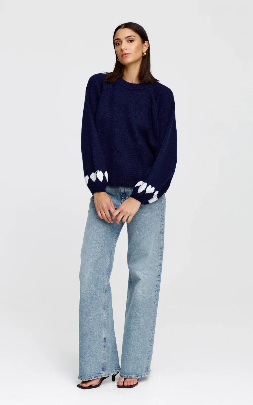 Navy blue knit sweater with white heart pattern on sleeves, paired with light wash wide-leg jeans