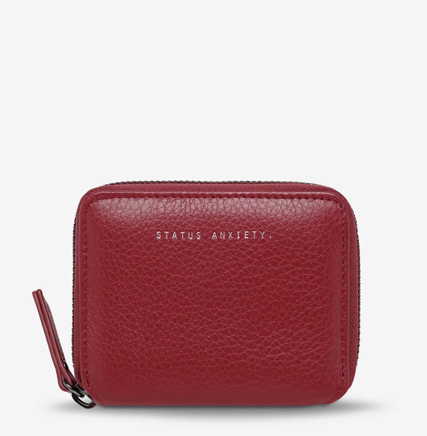 Red textured leather zip-around wallet with 'STATUS ANXIETY' branding, compact everyday accessory