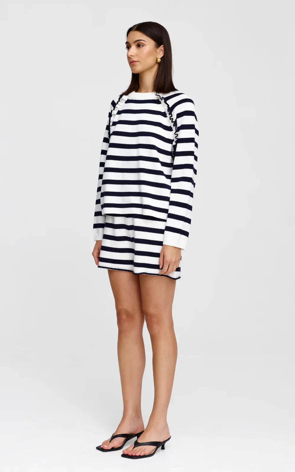 Woman in navy and white striped knit dress with ruffle shoulders, paired with black heeled sandals