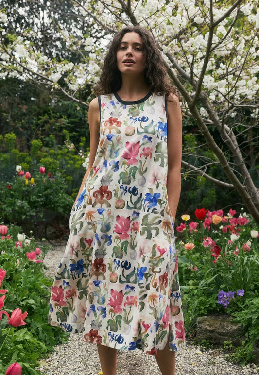Woman in a sleeveless floral print dress standing in a blooming garden with colorful flowers