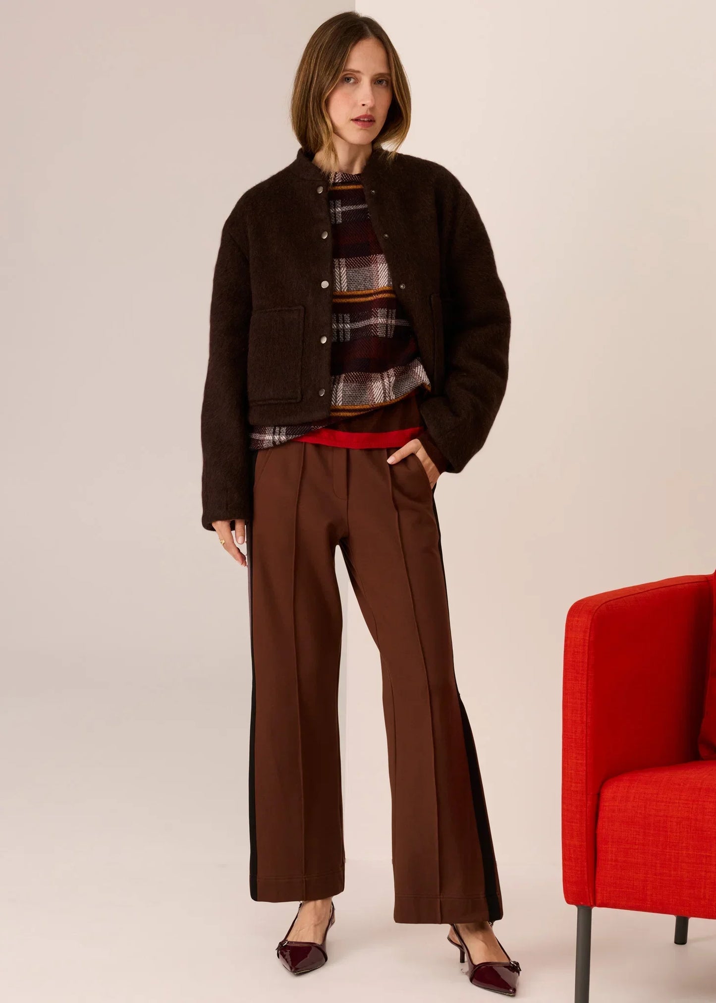 Woman in brown fuzzy jacket, plaid top, wide-leg trousers, and burgundy heels, styled for autumn fashion.
