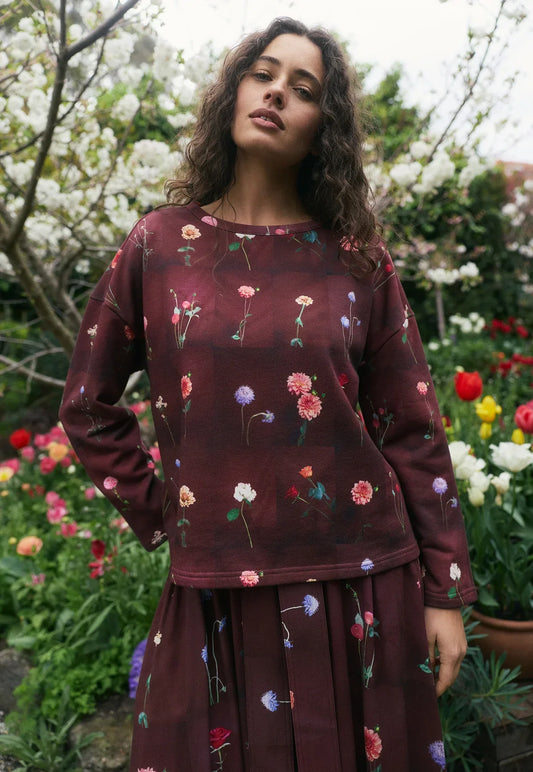 Woman in floral print burgundy top and skirt posing in a blooming garden