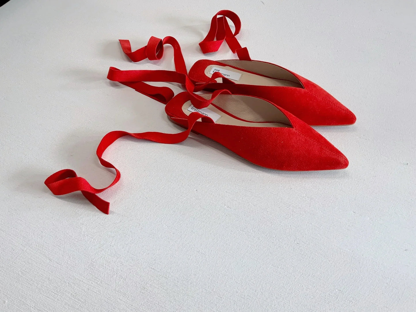 Red suede pointed-toe ballet flats with elegant tie ribbon straps.
