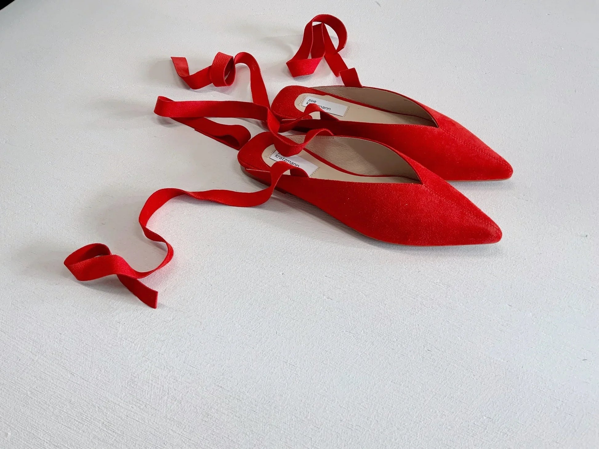Red suede pointed-toe ballet flats with elegant tie ribbon straps.