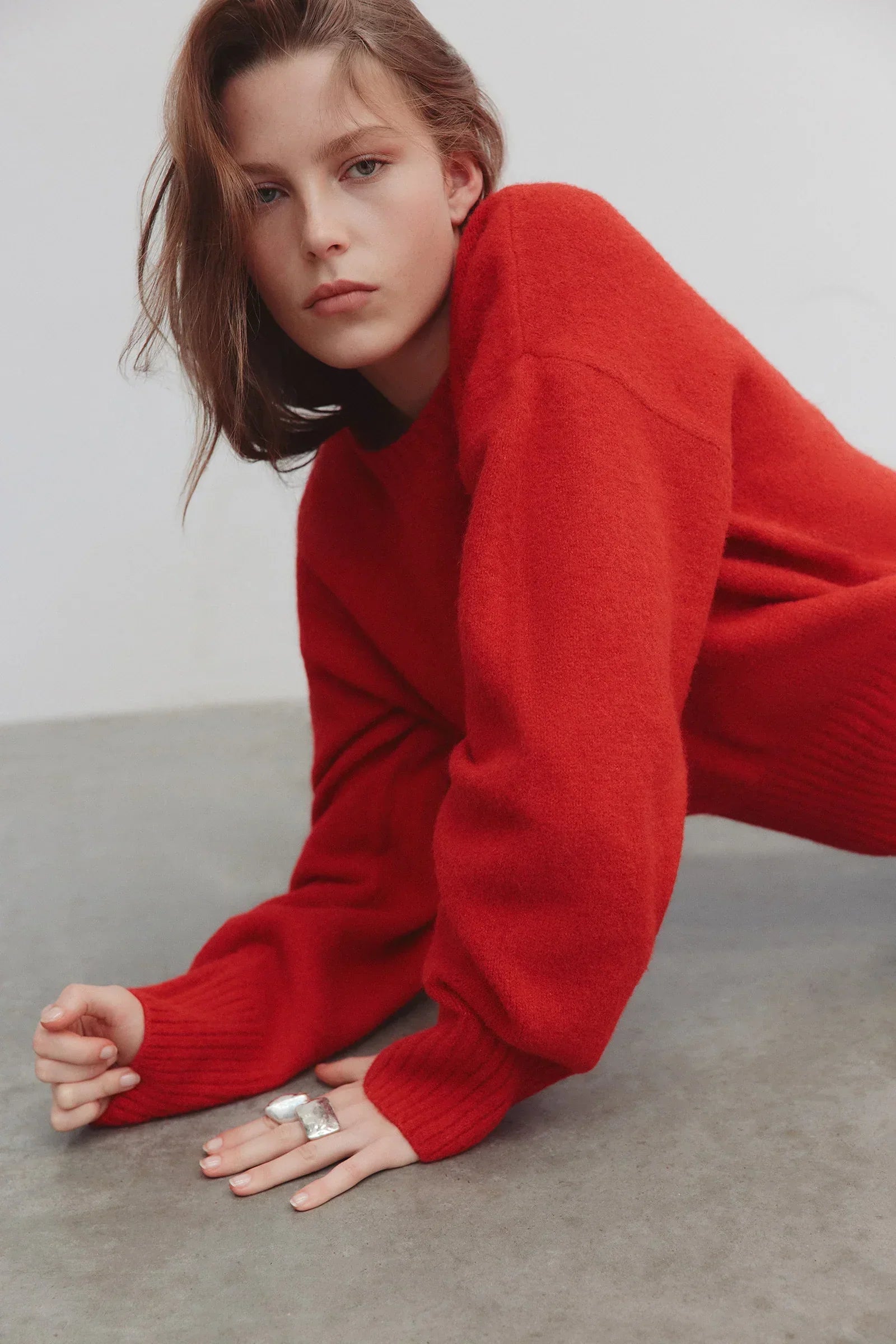 Woman in a bright red oversized knit sweater posing against a white background.