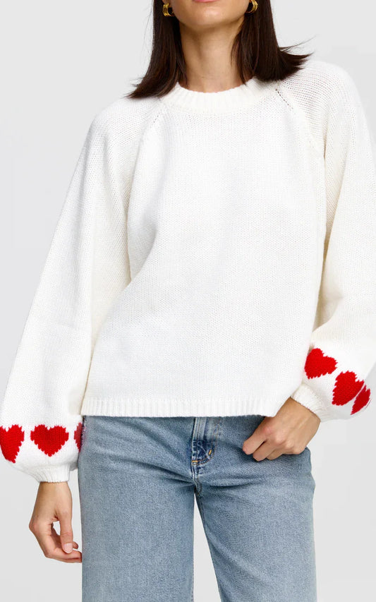 White knit sweater with red heart pattern on sleeves, paired with blue jeans