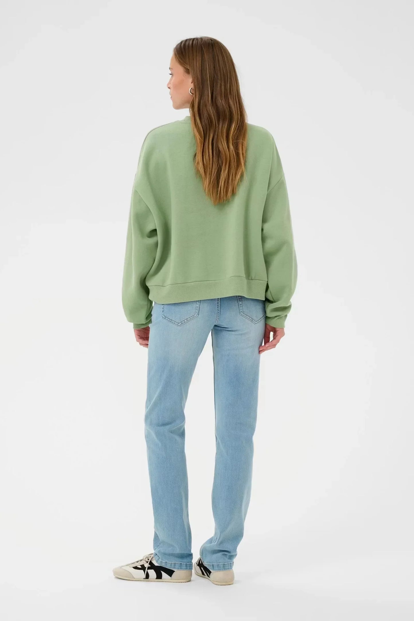 Woman wearing green oversized sweatshirt, light blue jeans, and sneakers, back view