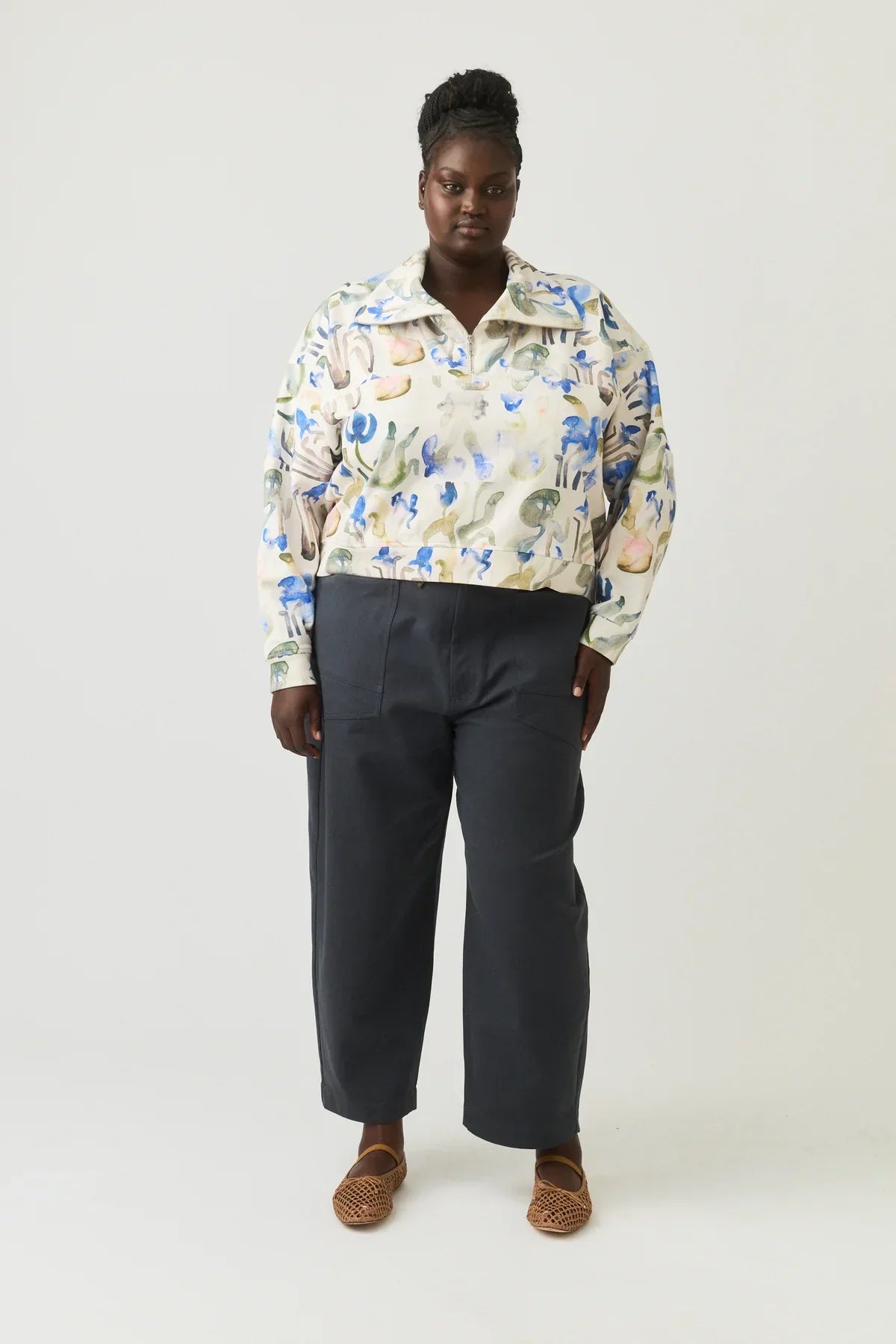 Woman wearing abstract print blouse, dark wide-leg pants, and woven flats, standing indoors