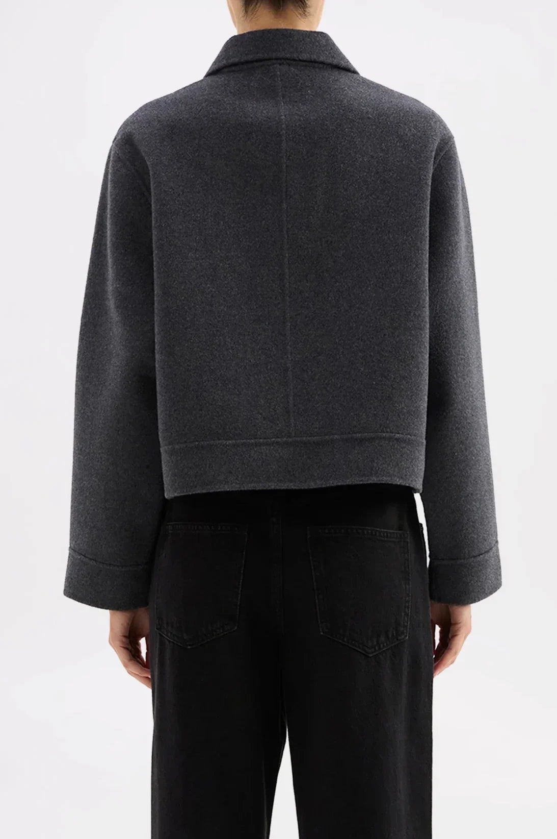 Back view of a woman wearing a dark gray cropped wool jacket with cuffed sleeves, paired with black wide-leg jeans.