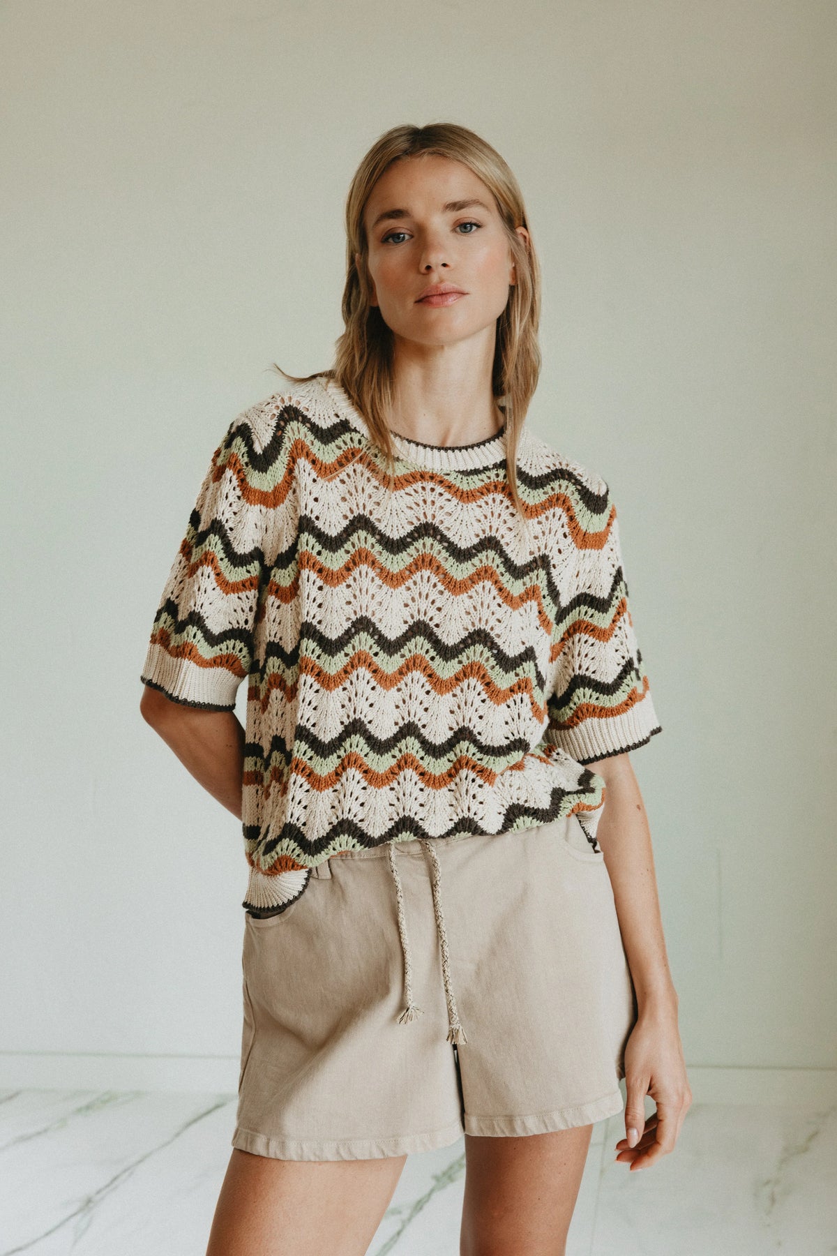 Woman wearing an INDI & COLD Zig Zag Crochet Short Sleeve Sweater and beige shorts.