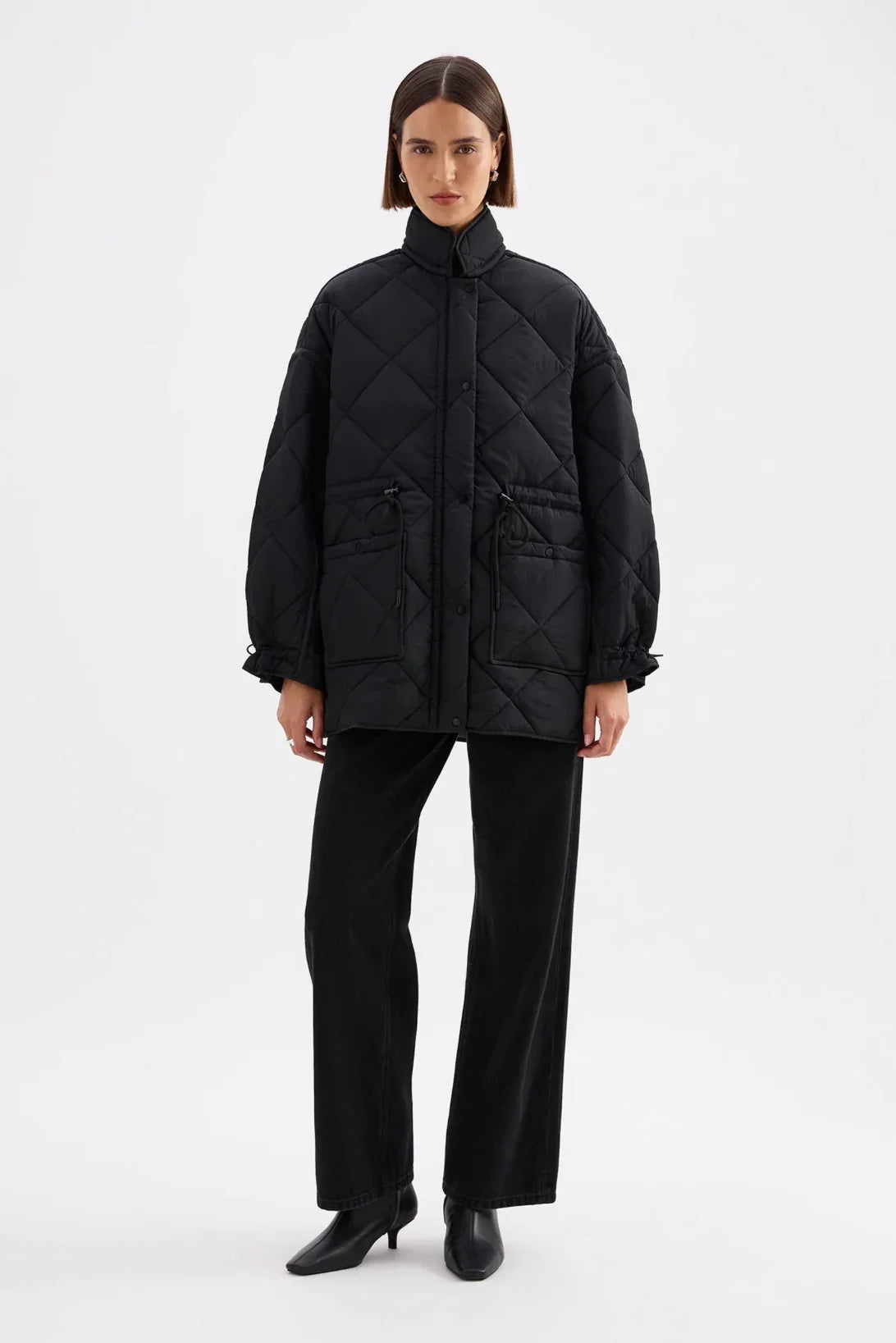 Black quilted puffer jacket with drawstring pockets, styled with black wide-leg pants and heels