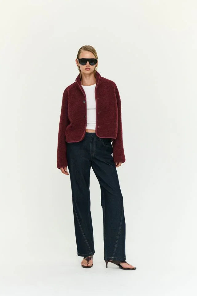 Woman in burgundy teddy jacket, white top, wide-leg jeans, and heeled sandals