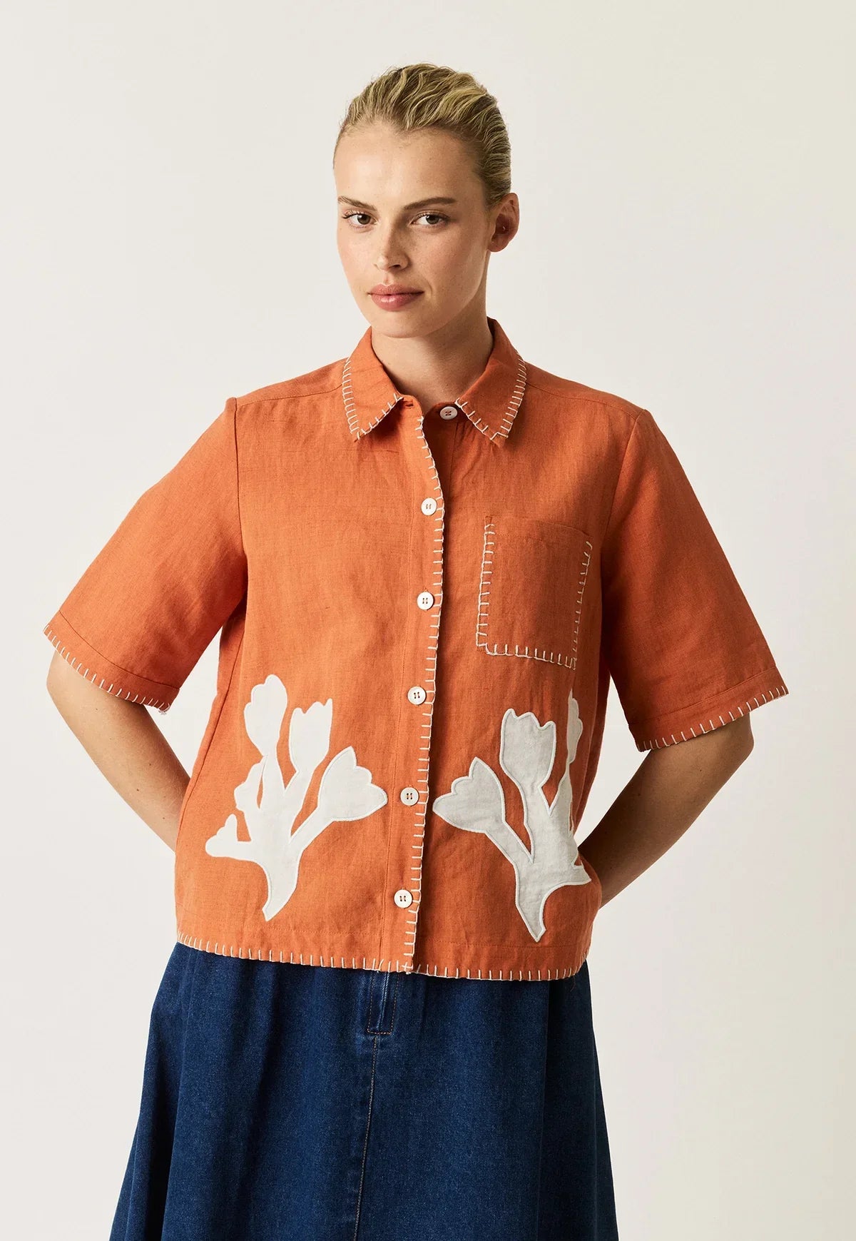 Woman wearing a NANCYBIRD Summer Shirt in Blossom Appliqué in orange with white floral details.