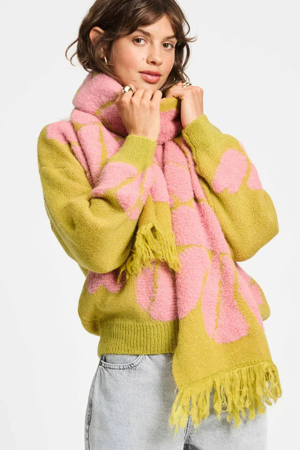 Woman wearing a chunky knit green sweater with pink floral pattern and matching fringed scarf
