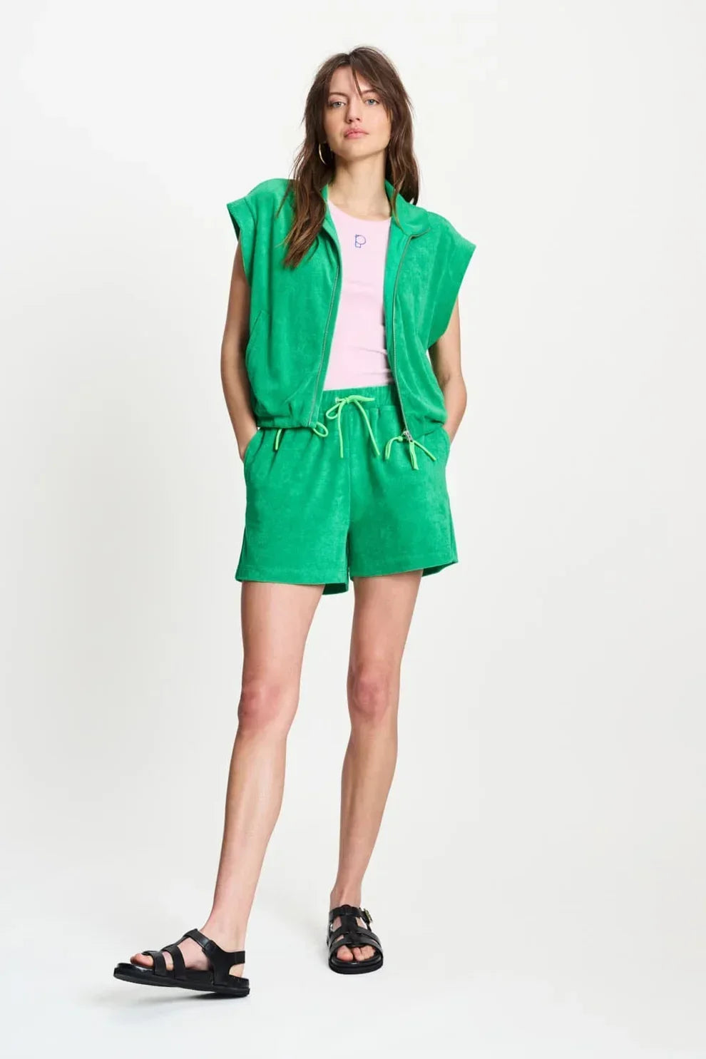 Woman wearing a green sleeveless zip-up top and matching green shorts with black sandals.