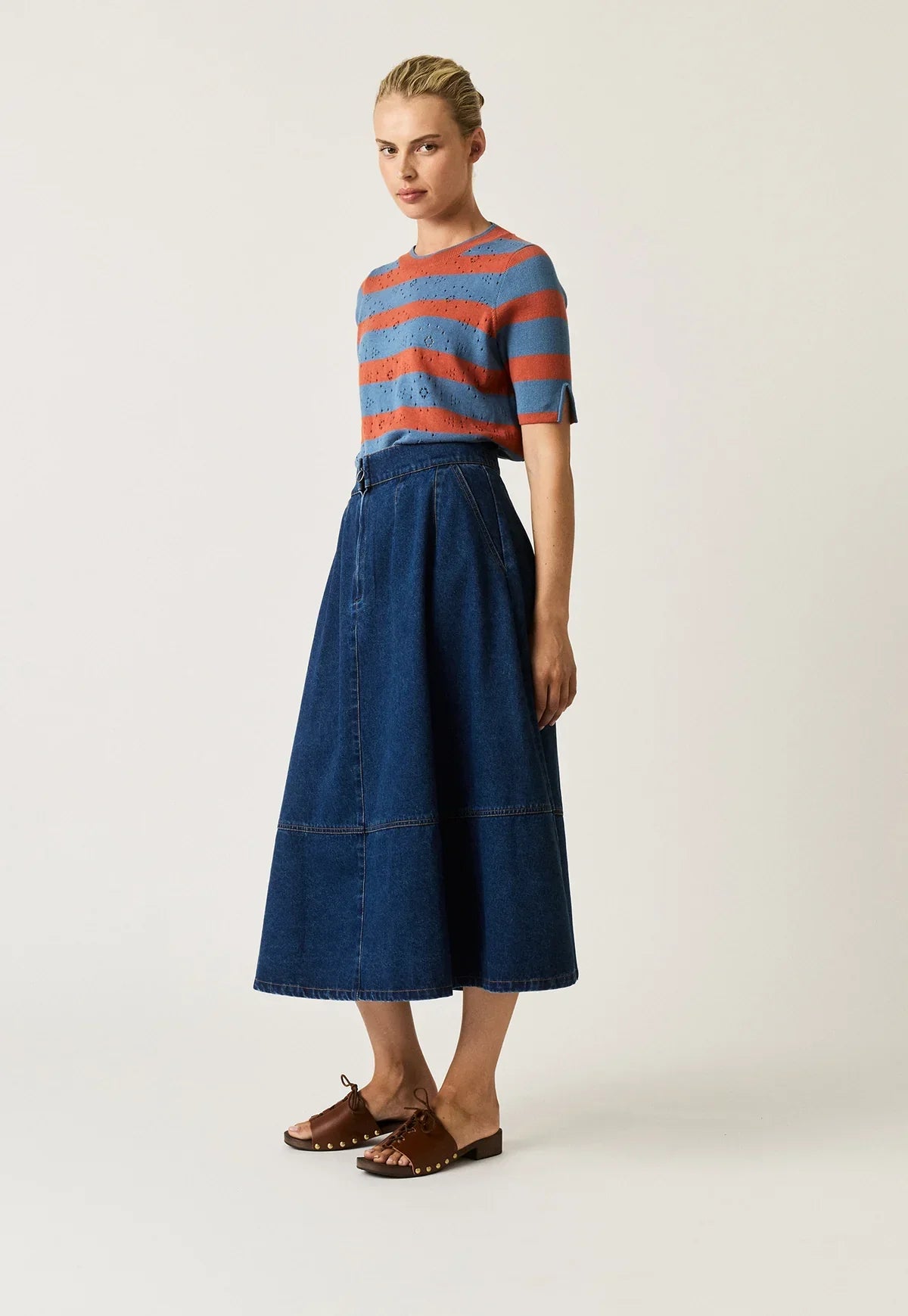 Woman wearing NANCYBIRD Aries Denim Skirt in dark wash with a striped knit top and brown sandals